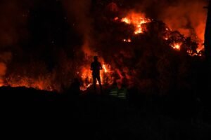 Dramática escena nocturna en la que tres siluetas de bomberos forestales observan las llamas devorar la vegetación del bosque. | Özgür Sürmeli, Pexels.