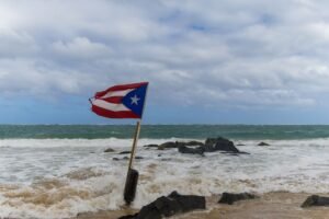 Bandera de Puerto Rico ante el embate del oleaje en una playa. Phil Evenden, Pexels.